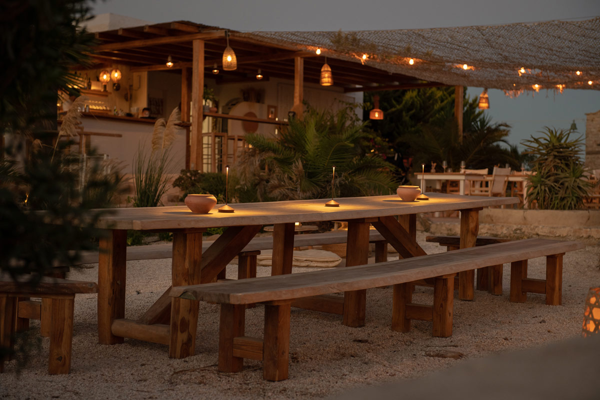 Sunset Antiparos | Restaurant in Antiparos, Greece | Photograph of long wooden table in foreground and outdoor restaurant in background